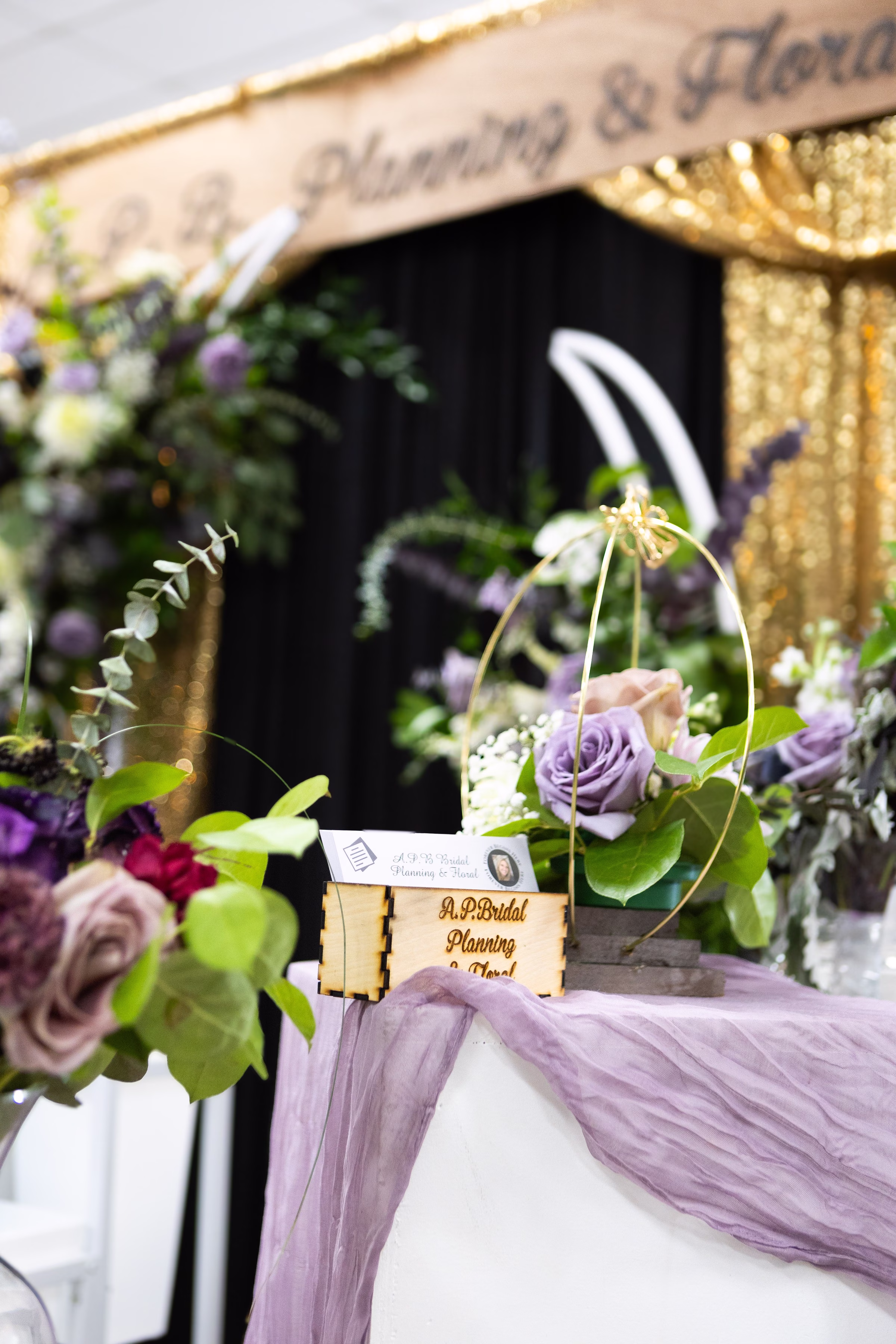 ap bridal planning floral booth puyallup wedding show - Exhibiting Information A.P. Bridal Planning and Floral vendor booth display featuring purple and mauve roses with gold accents and laser-engraved wooden business card holder at the Puyallup Wedding Show in Puyallup Washington