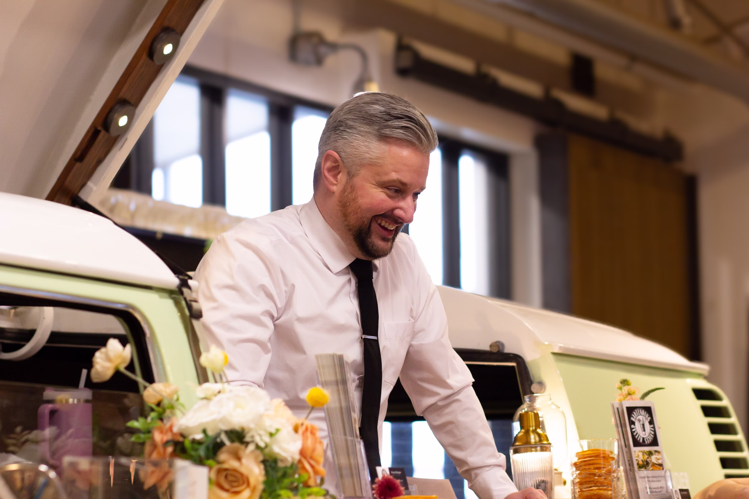 bartender vintage vw van bar puyallup wedding show - The Puyallup Wedding Show A smiling bartender in a white shirt and black tie serves drinks from a mint green vintage VW van bar surrounded by floral arrangements at the Puyallup Wedding Show in Puyallup Washington