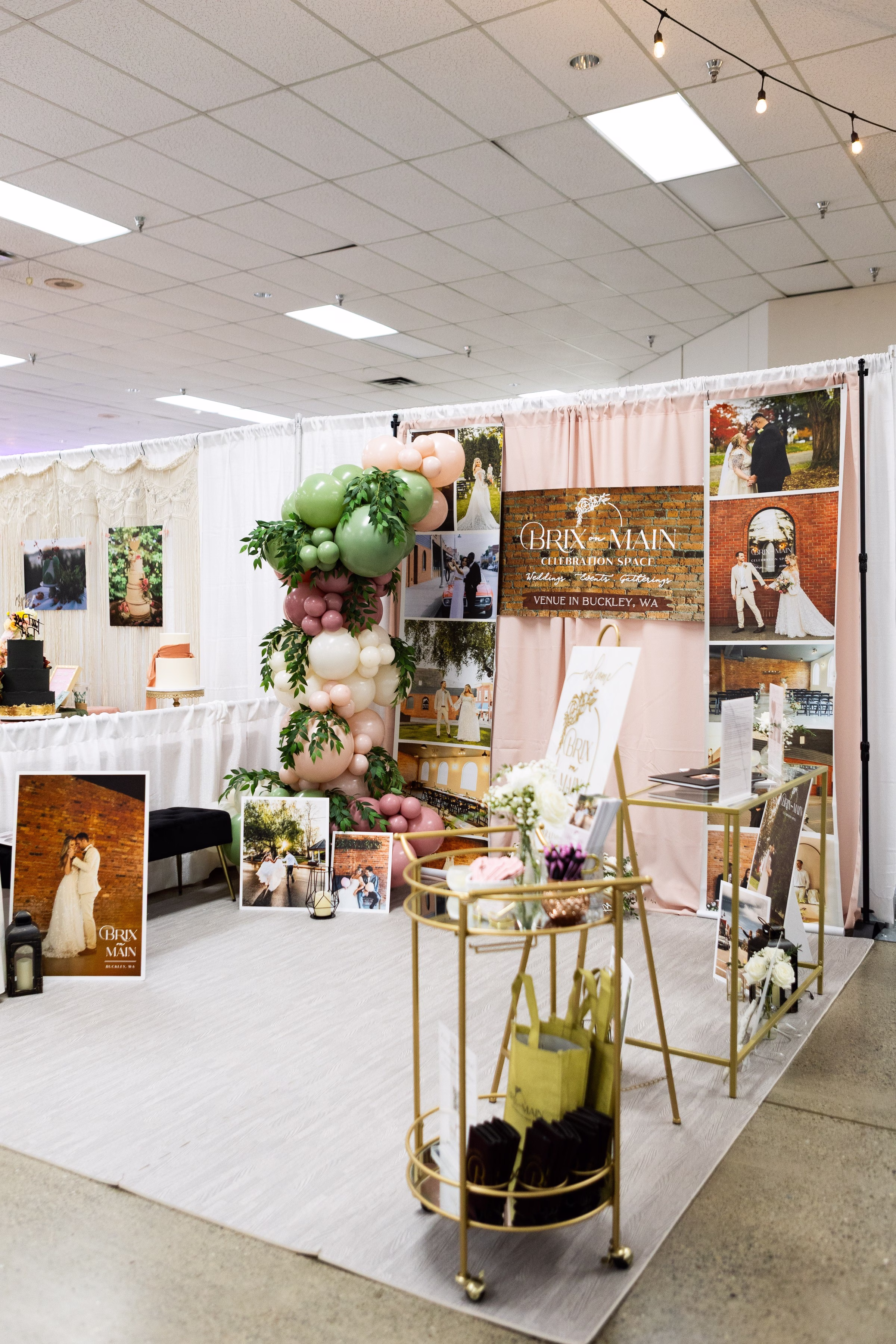 brix on main wedding venue bridal show booth buckley wa - The Puyallup Wedding Show Brix on Main Celebration Space wedding venue booth at the Puyallup Wedding Show in Washington, featuring a balloon garland arch, wedding photos, and gold bar cart display