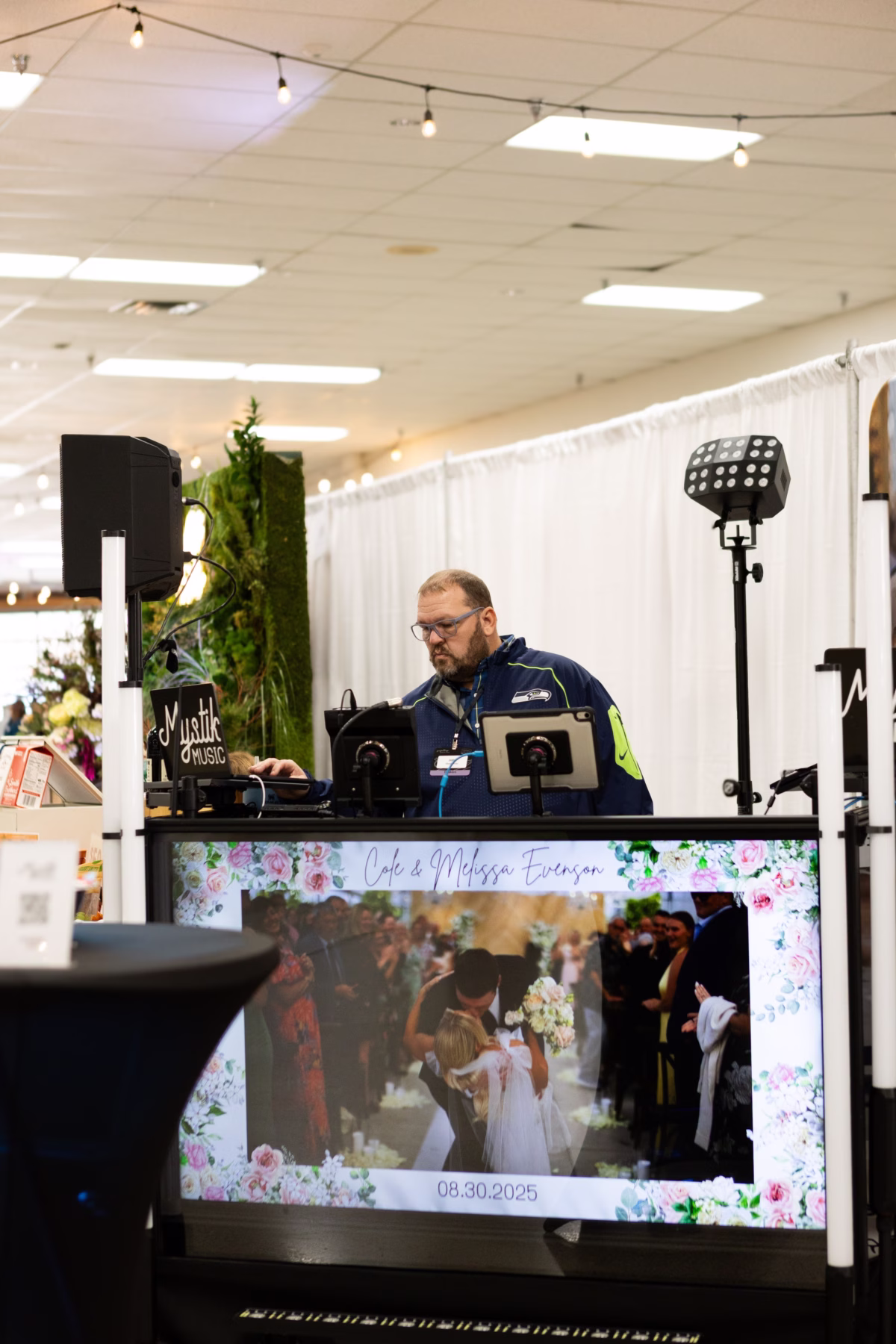 Mystik Music DJ setting up a professional wedding DJ booth with custom couple display screen at the Puyallup Wedding Show in Puyallup Washington