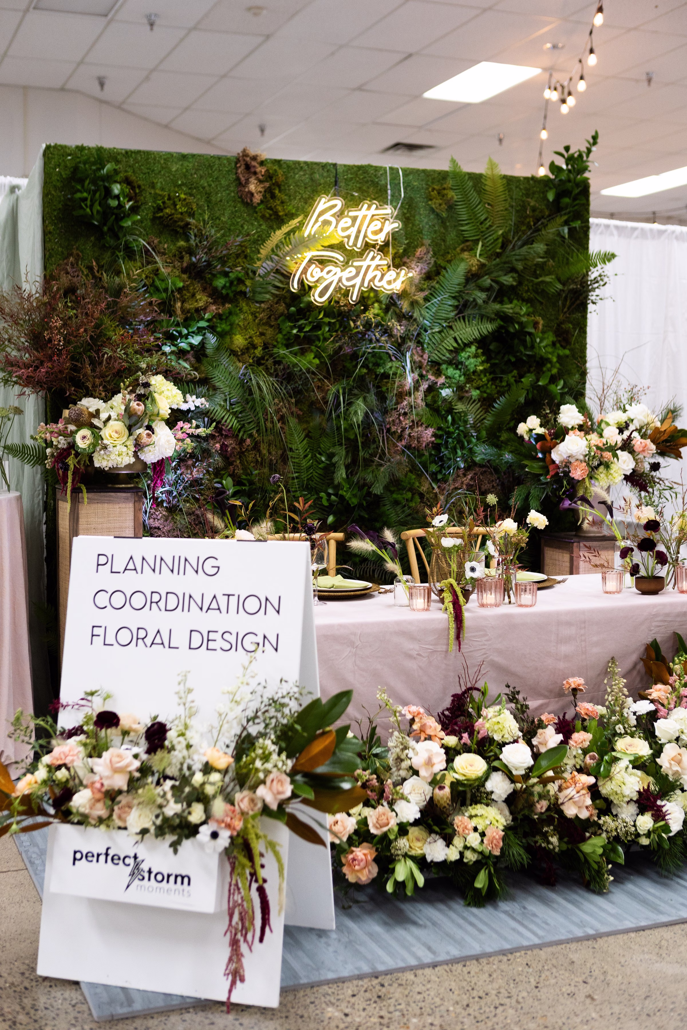 perfect storm moments wedding planning floral design puyallup - The Puyallup Wedding Show Perfect Storm Moments wedding planning coordination and floral design booth display with lush greenery wall, neon Better Together sign, and elegant blush pink tablescape with florals at a Puyallup Washington bridal show