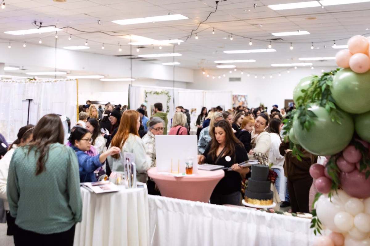 Engaged couples and wedding vendors networking at the Puyallup Wedding Show bridal expo in Puyallup Washington, featuring balloon arch decor and vendor display tables