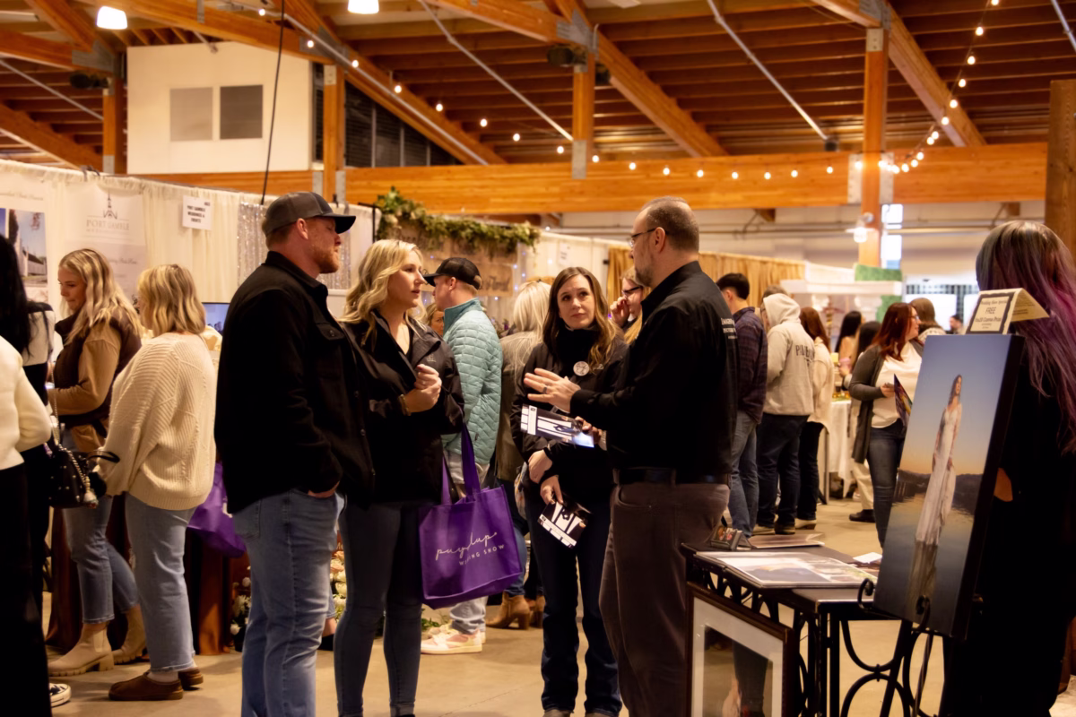 puyallup wedding show bridal expo vendor networking washington - February 2027 Couples and vendors networking at the Puyallup Wedding Show bridal expo in Puyallup Washington, with attendees carrying branded purple tote bags while browsing wedding vendor booths