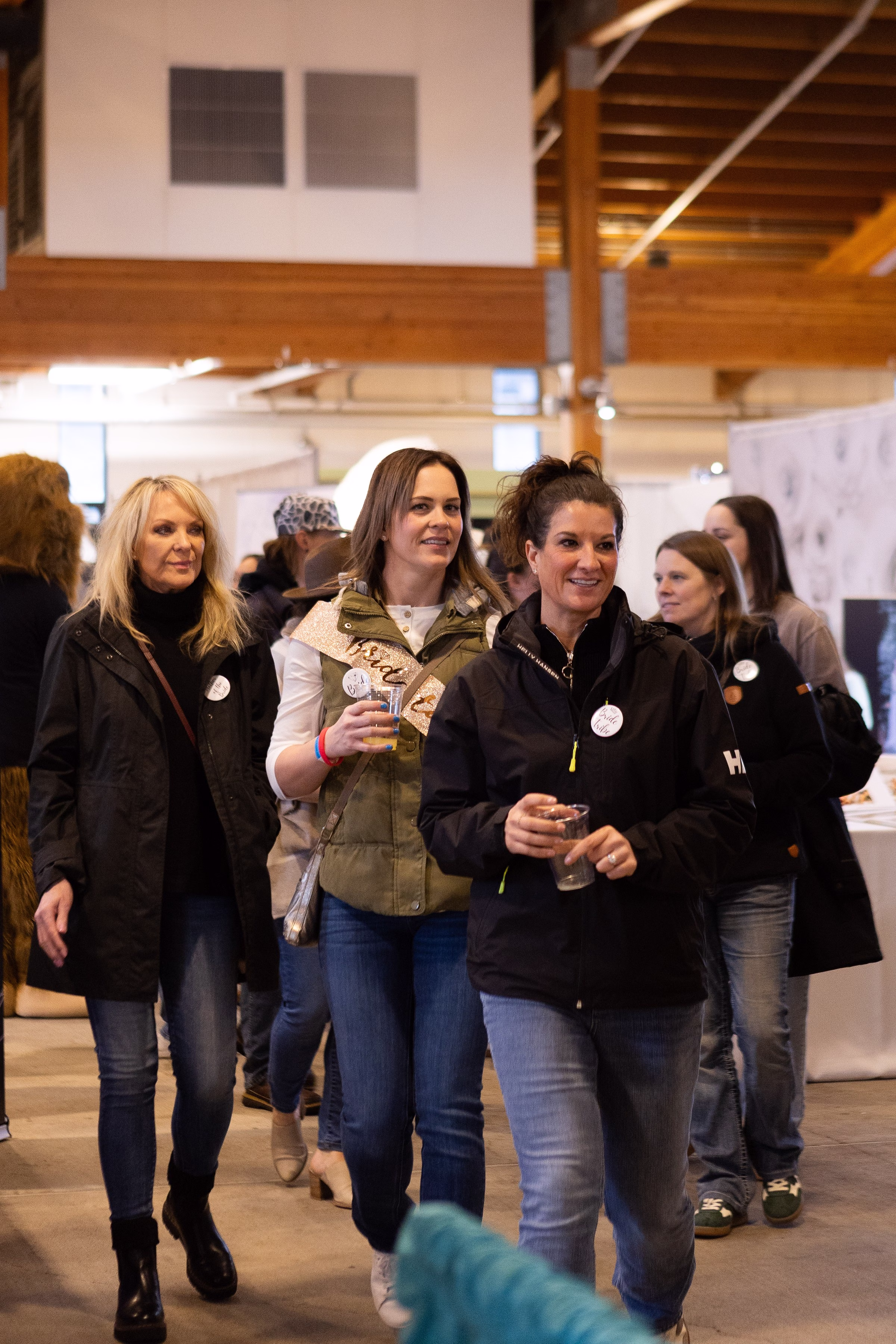 puyallup wedding show bridal party attendees exploring venue - Exhibiting Information Bridal show attendees including a bride-to-be holding a decorative sash walk through the Puyallup Wedding Show event hall in Puyallup Washington