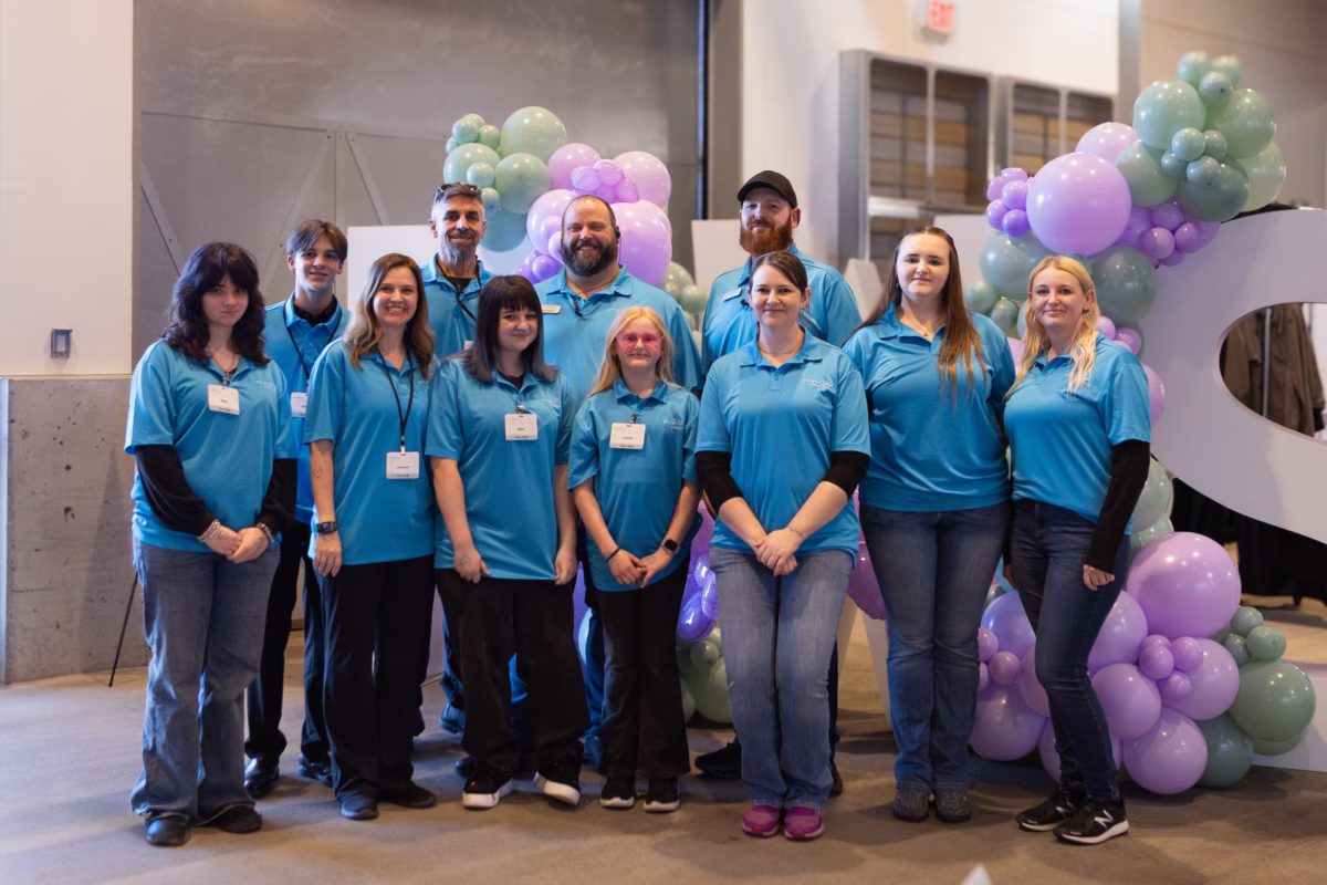 puyallup wedding show staff team bridal event - Upcoming Shows The Puyallup Wedding Show team members wearing matching teal polo shirts pose together in front of a purple and green balloon arch display at the Puyallup Washington bridal show