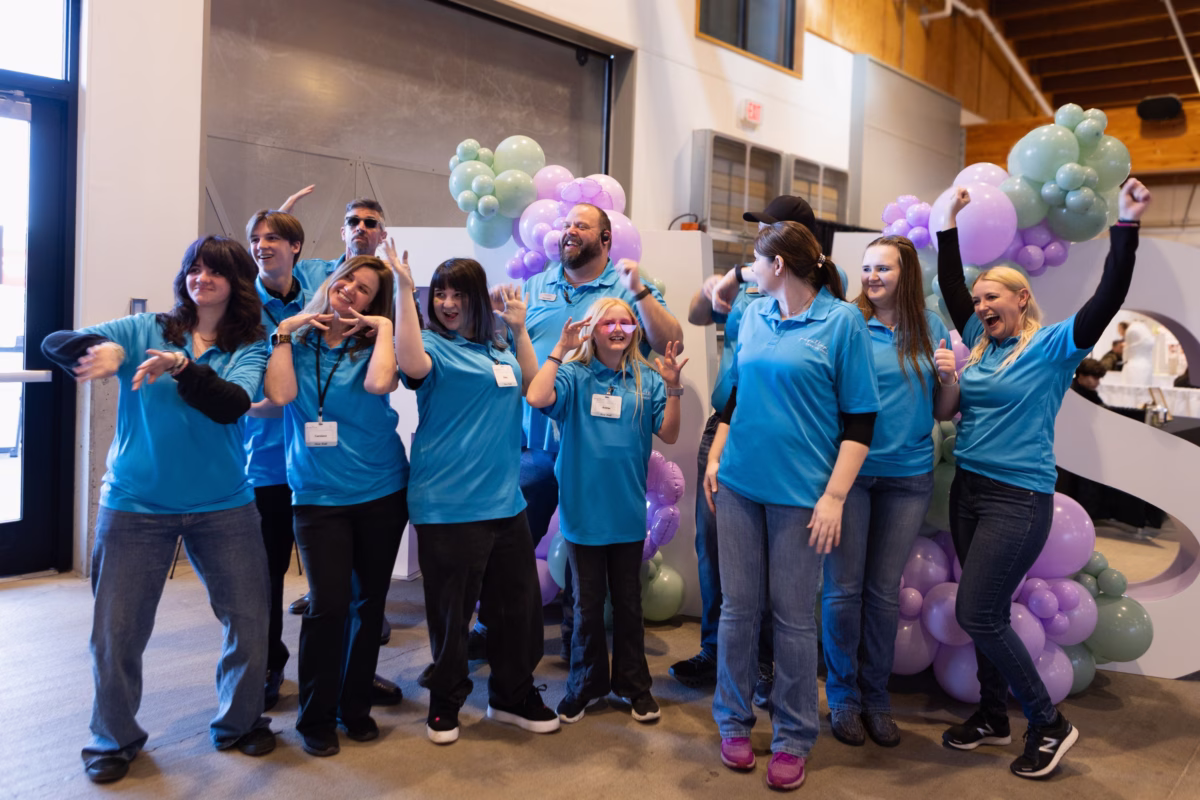 The Puyallup Wedding Show staff team celebrating in matching blue polo shirts at the Puyallup Washington bridal show venue surrounded by purple and green balloon decorations