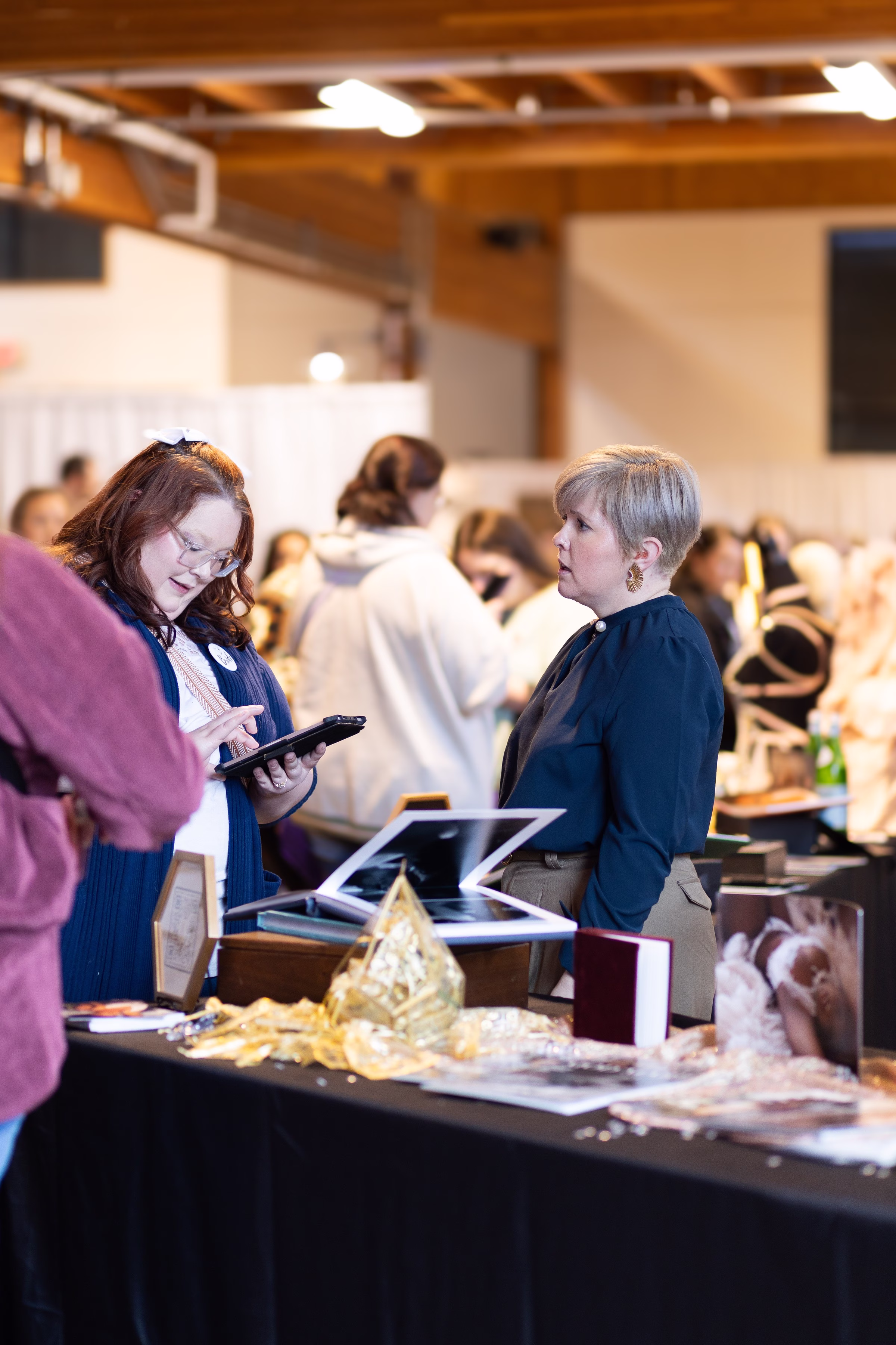 puyallup wedding show vendor booth bridal fair - The Puyallup Wedding Show A vendor at the Puyallup Wedding Show in Puyallup Washington uses a tablet to assist a bride at a display table featuring framed photos and decorative items at a bridal show vendor booth